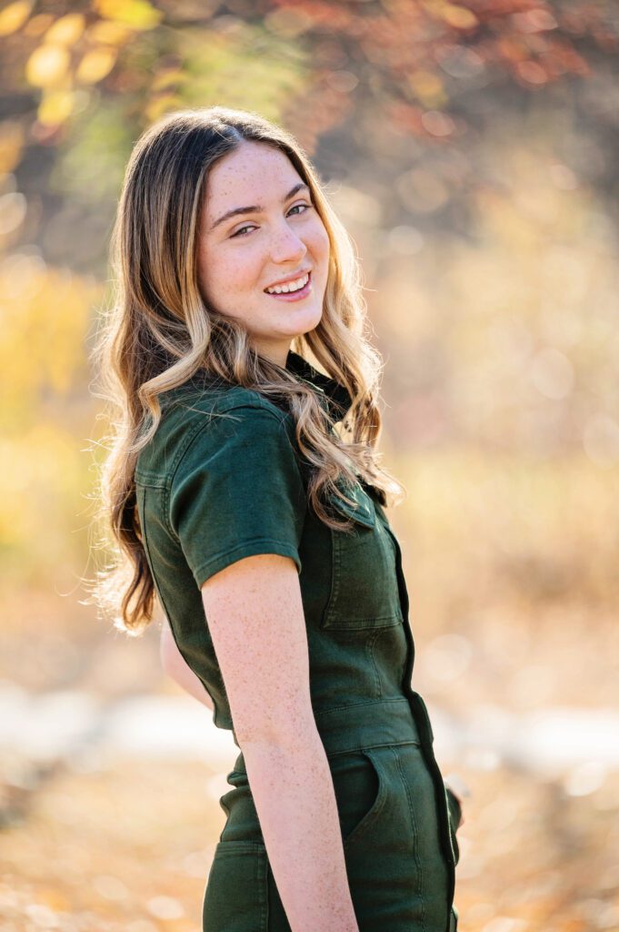 Senior pictures in Edina by Elissa Bean Photography featuring a smiling high school senior in a green jumpsuit with golden fall foliage in the background.
